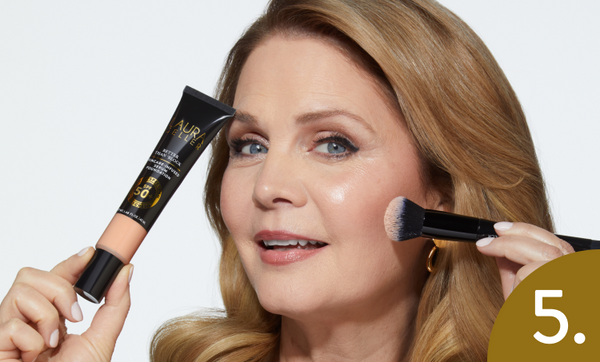 Woman applying Laura Geller Better Than Block with a brush and a tube of cream, against a white background.
