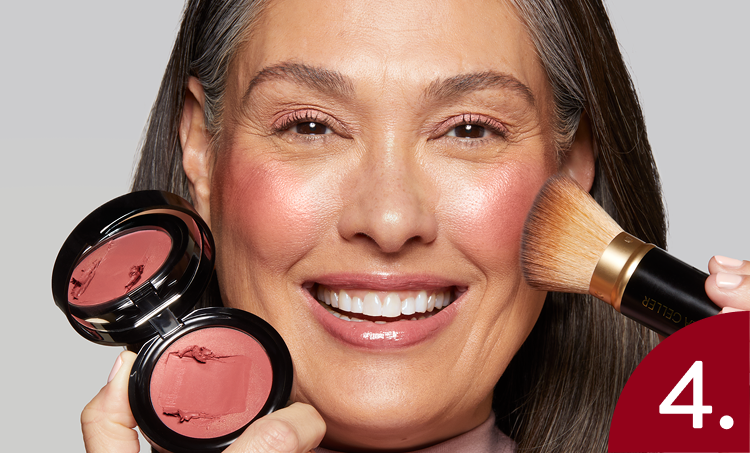 Woman applying Laura Geller Wonder Balm with a brush on a gray background
