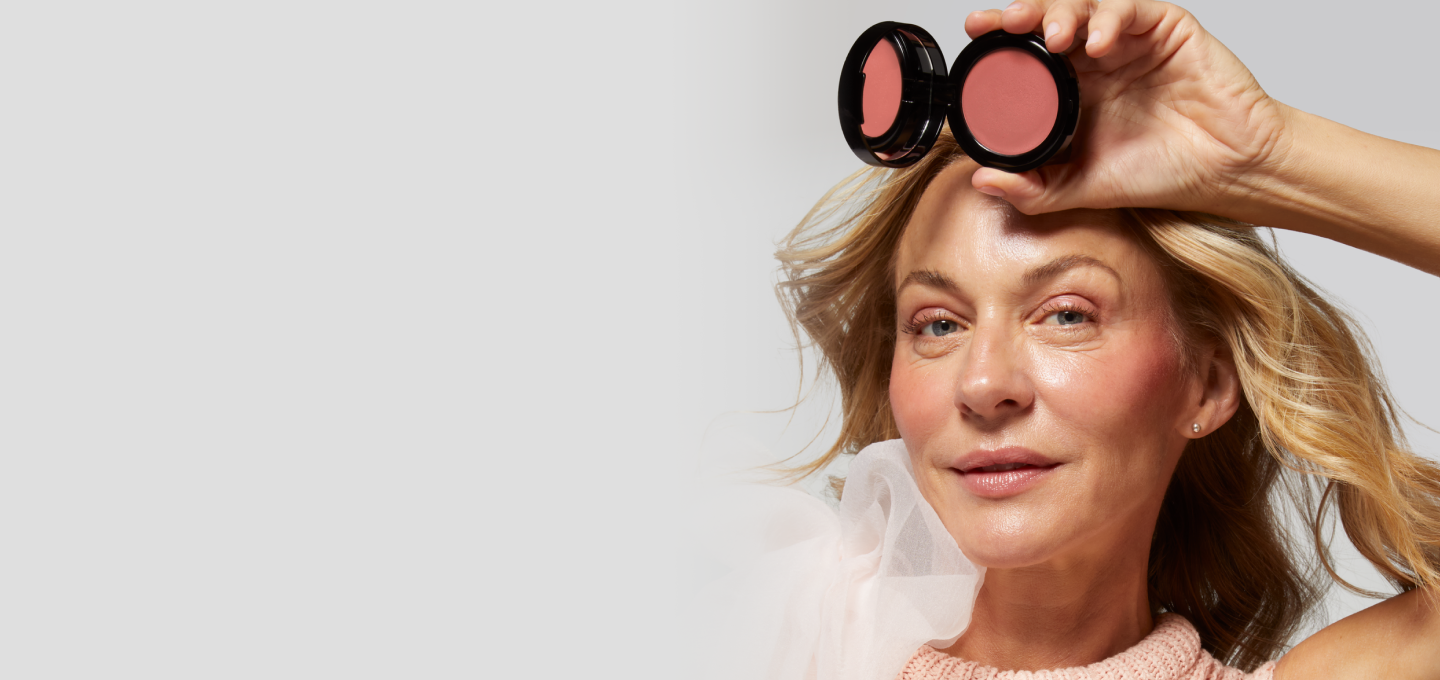 Woman holding Laura Geller Wonder Balm product above her eyes against a plain background