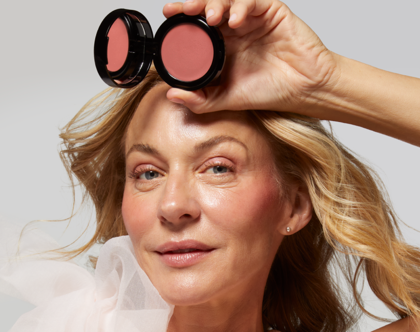 Woman holding Laura Geller Wonder Balm product above her eyes against a plain background