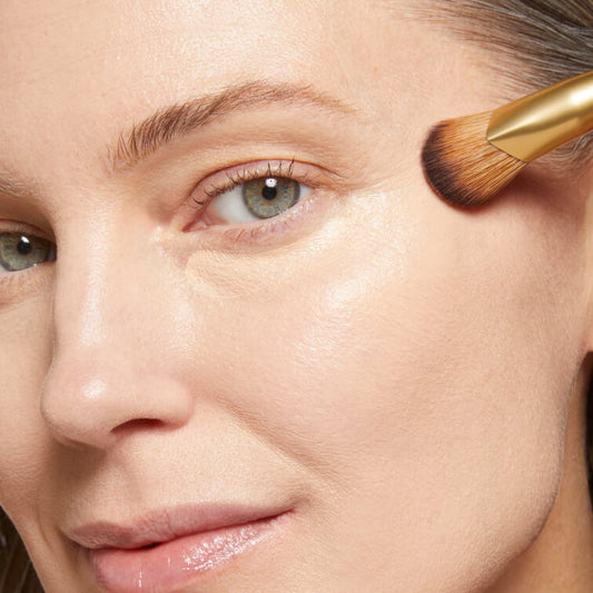 Macro shot of woman applying makeup with a brush on her cheek 