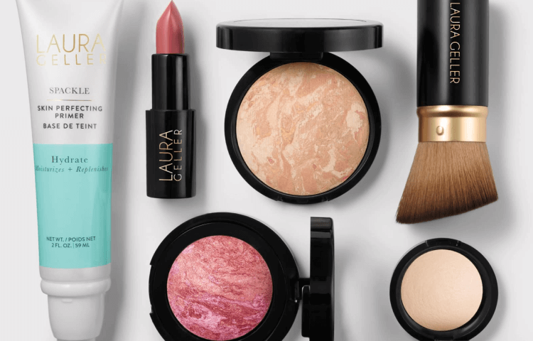 Laura Geller makeup products including primer, lipstick, blush, and brush on a white background
